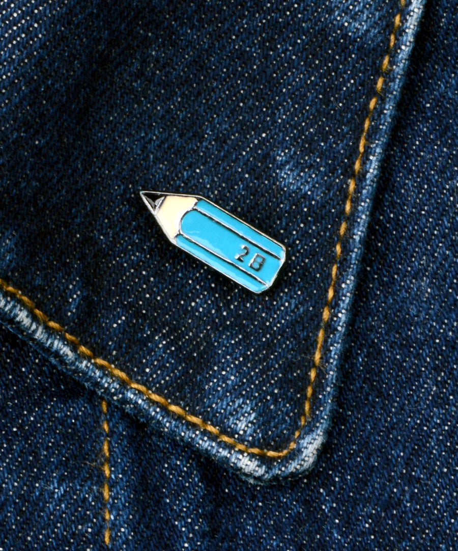 Kék ceruza alakú, pin jellegű kitűző.